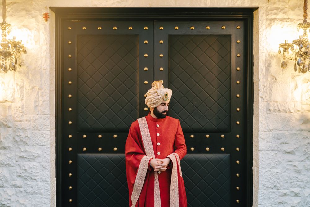 Photo of Classic groom portrait with groom in an all-red sherwani with gold details and a matching gold pagdi
