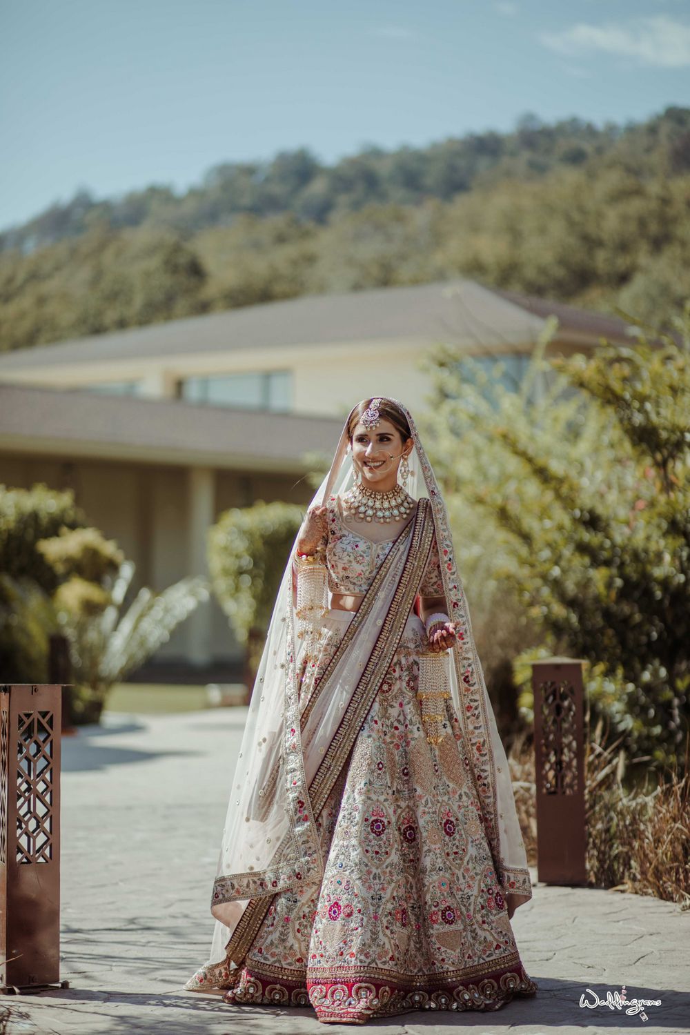 Photo of bride in a white lehenga with maroon border and floral motifs