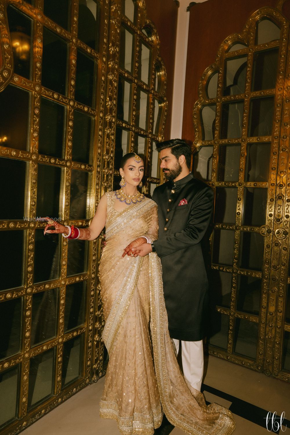 Photo of Stunning couple portrait with the groom in a classic black bandhgala and the bride in a gold net saree and a statement necklace