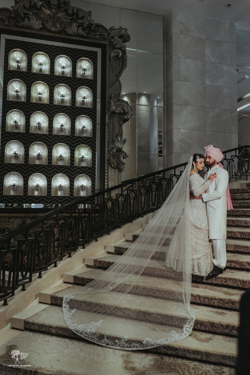 Photo of bride and groom portrait on stairs with trail lehenga dupatta