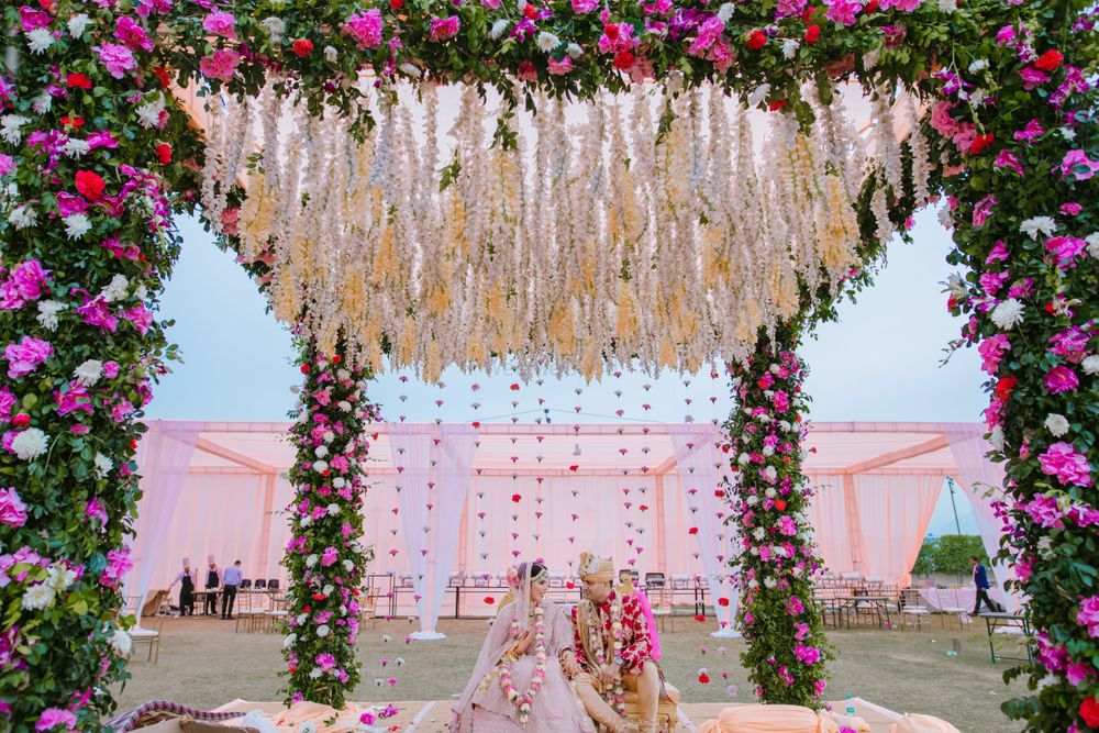 Photo of The bride and groom under a gorgeous floral mandap.