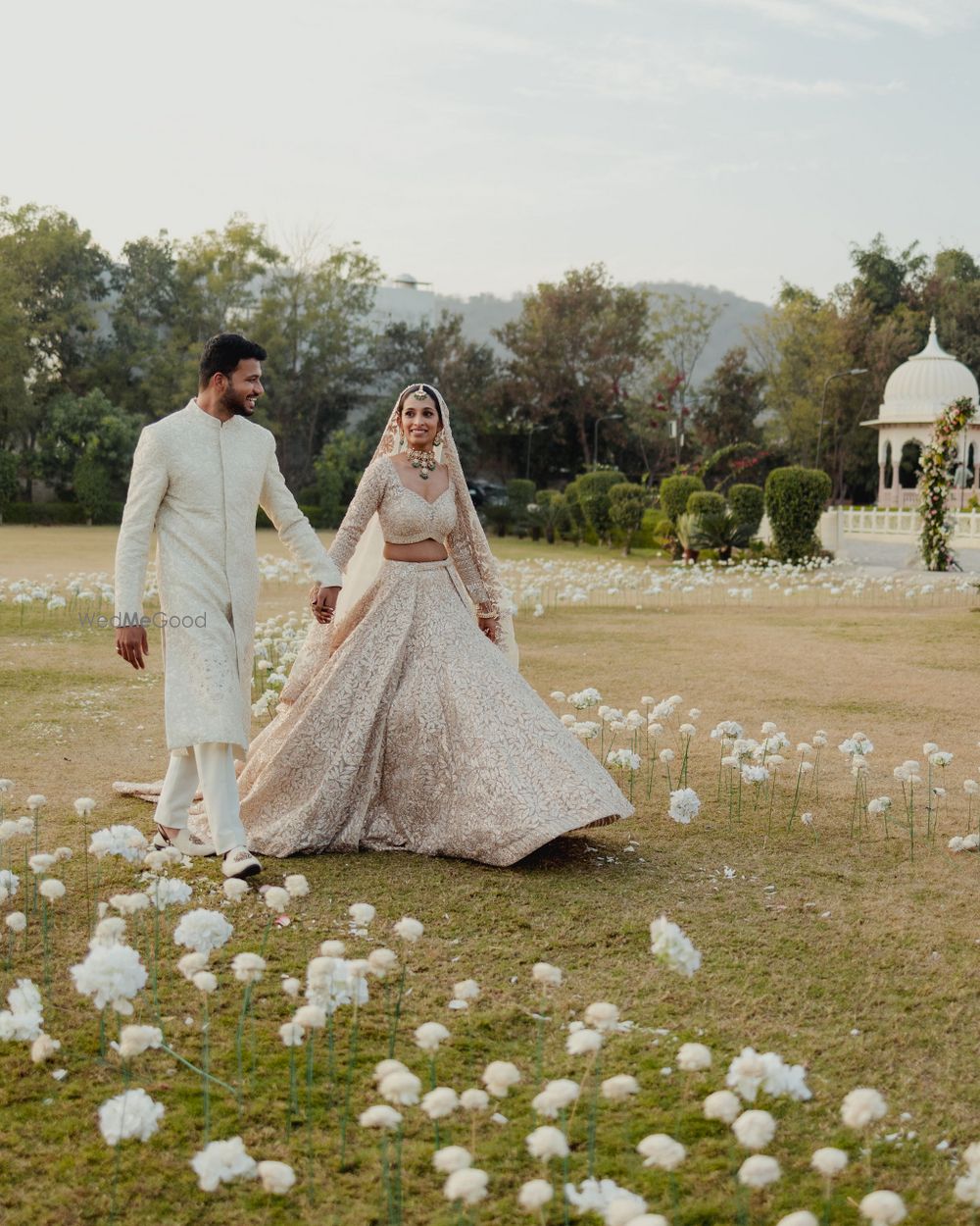 Photo of Gorgeous shot of the couple walking hand in hand between the aisle that is decorated with all-white floral single flower decor