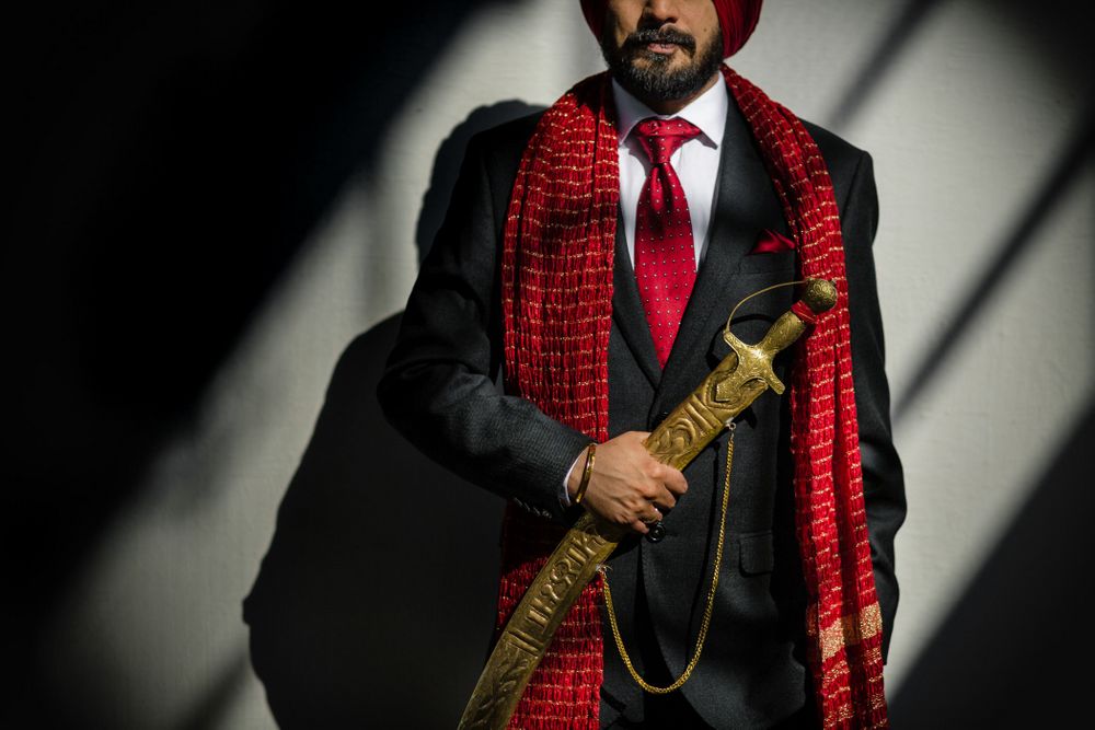 Photo of Photo of a groom wearing a black tuxedo with a red stole, a red tie and a red turban