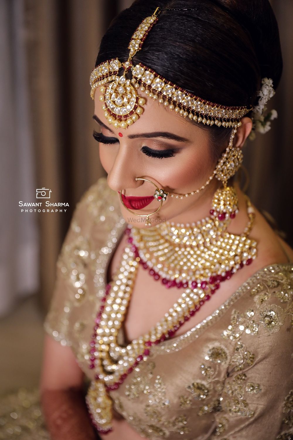 Photo of A bride sitting elegantly in a gold outfit, perfectly complimented by her gold and maroon jewelry. She is seen wearing a polki and jadau choker and a rani haar with gold and maroon beads and a maathi-patti in similar colors.