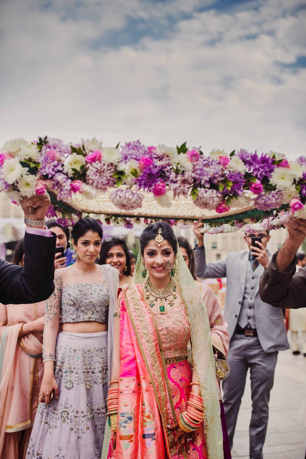 Photo of Bride entering her wedding in lehenga in paithani silk under a floral chaddar