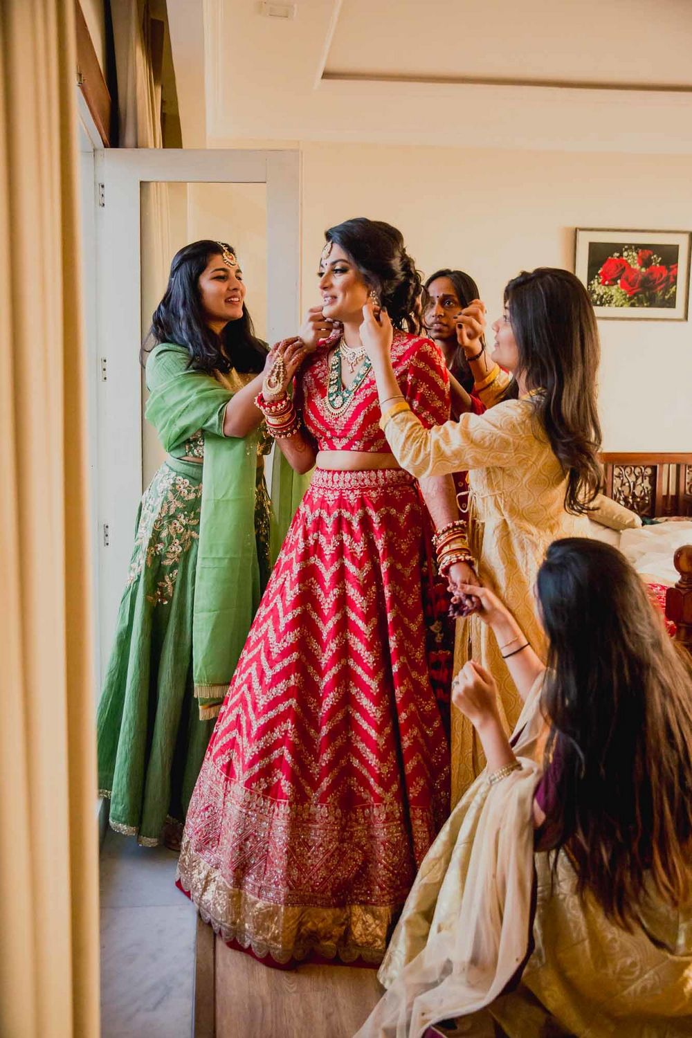 Photo of Bridesmaids help a bride in red get ready