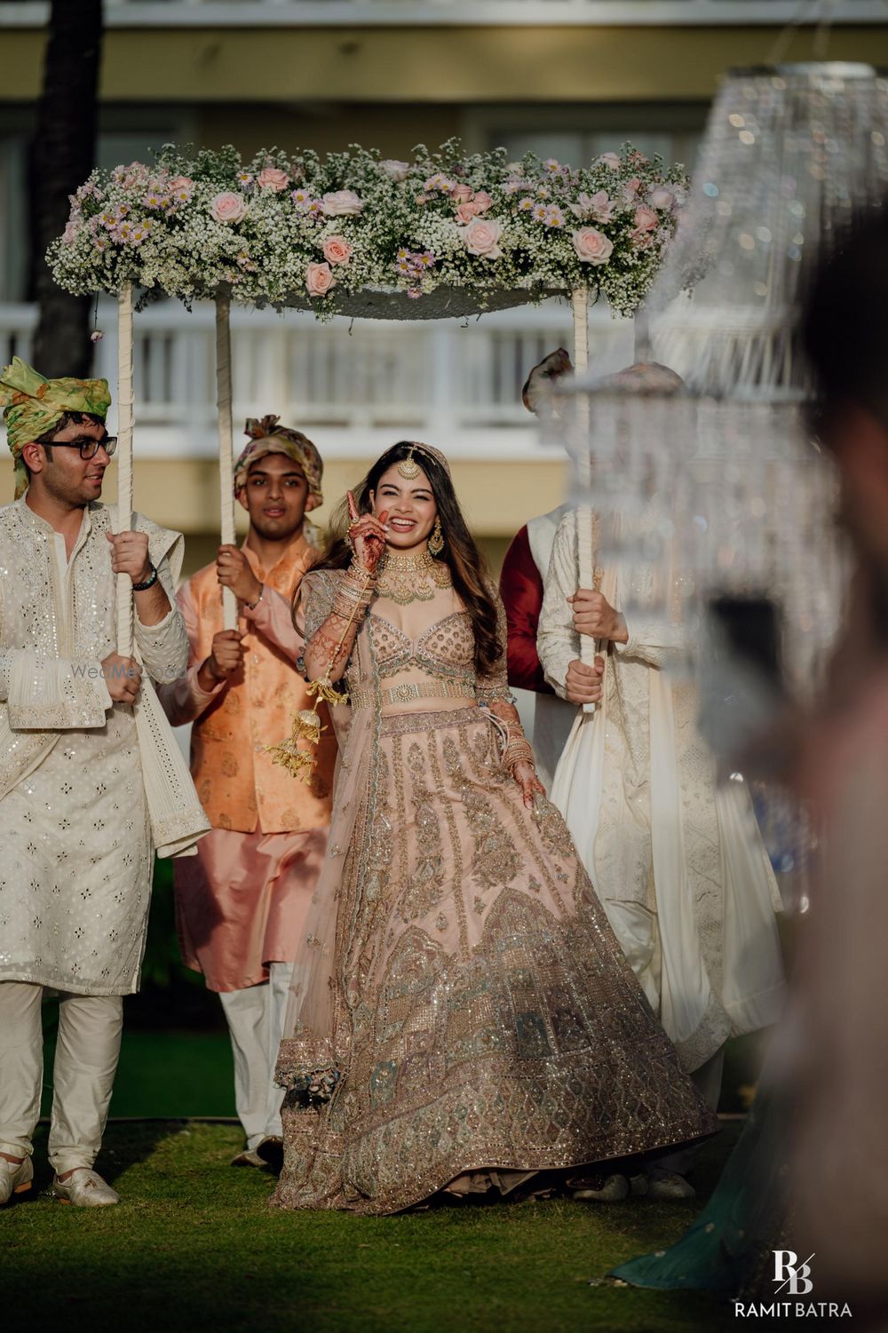 Photo of Gorgeous and dancing bride in a pastel lehenga entering the wedding venue under a phoolon ki chaddar