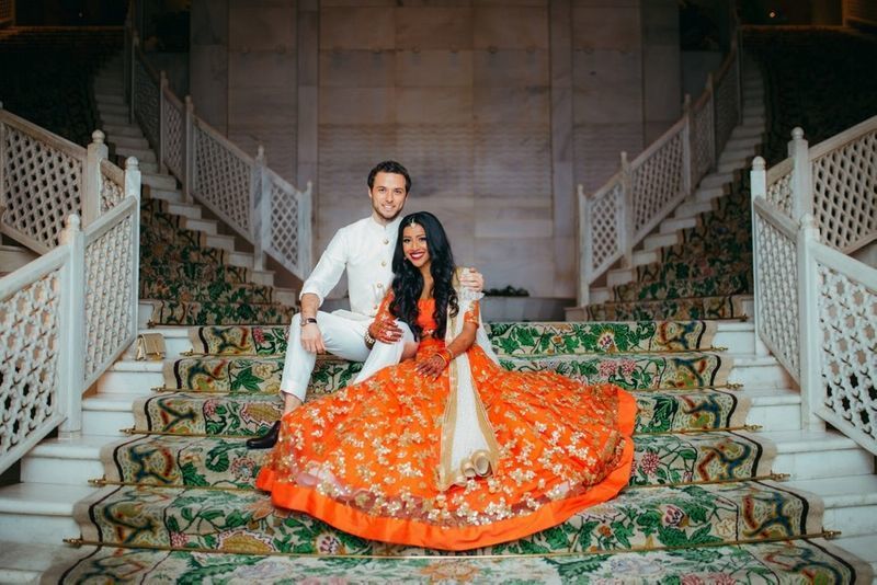 Photo of A bride in orange lehenga with her groom