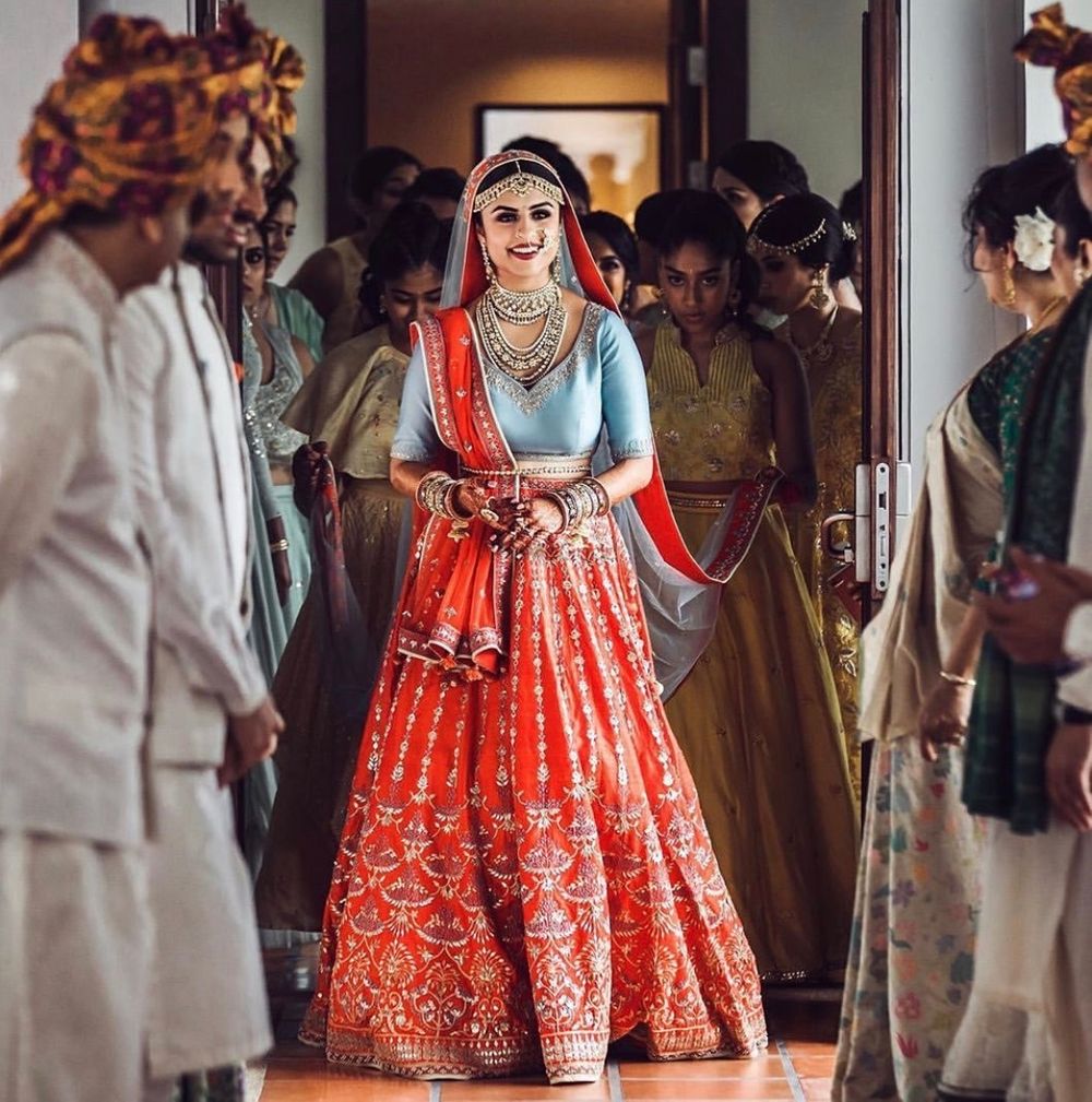 Photo of A bride in a tomato red lehenga with a contrasting blue blouse