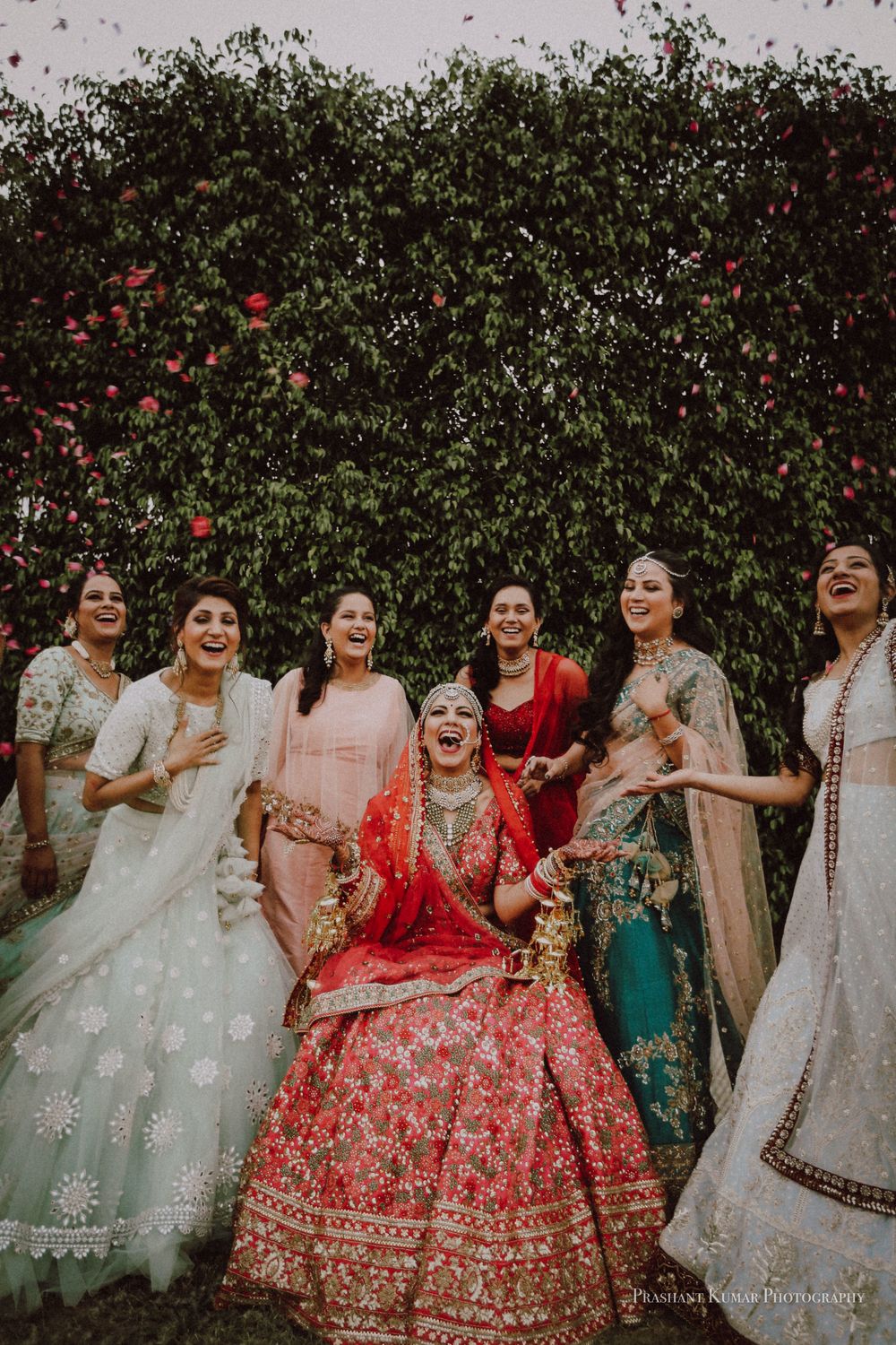 Photo of A bride in a red lehenga laughing with her bridesmaids on her wedding day