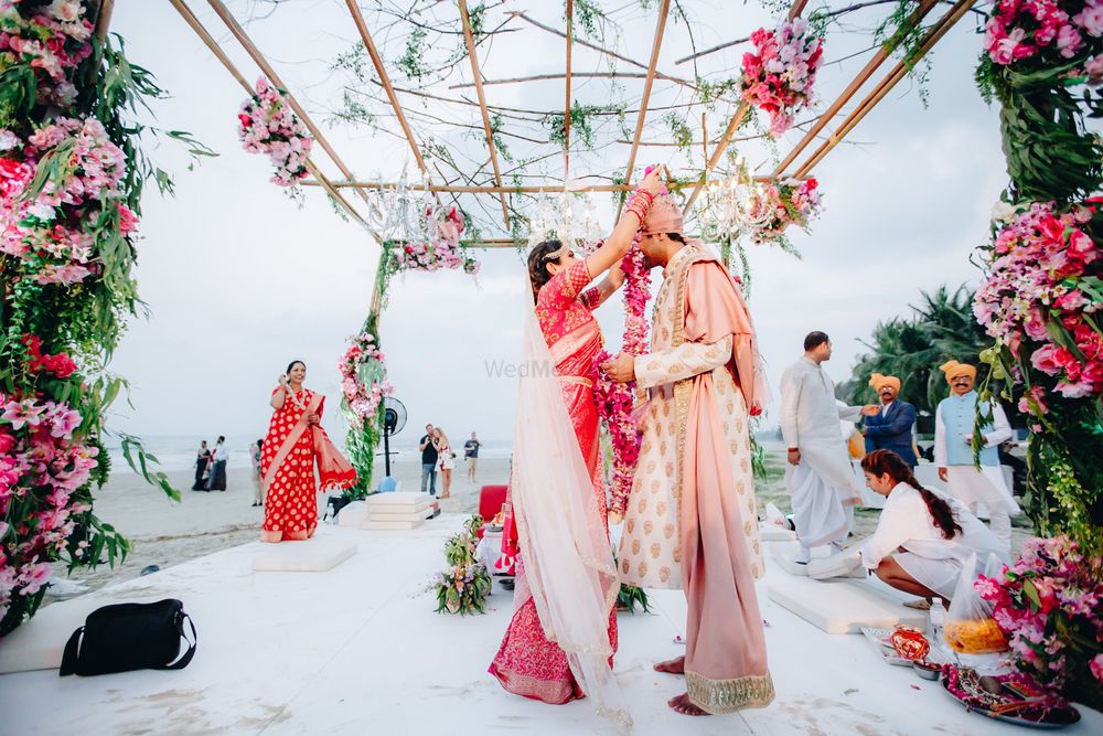 Photo of A bride and groom exchange varmalas in a floral mandap