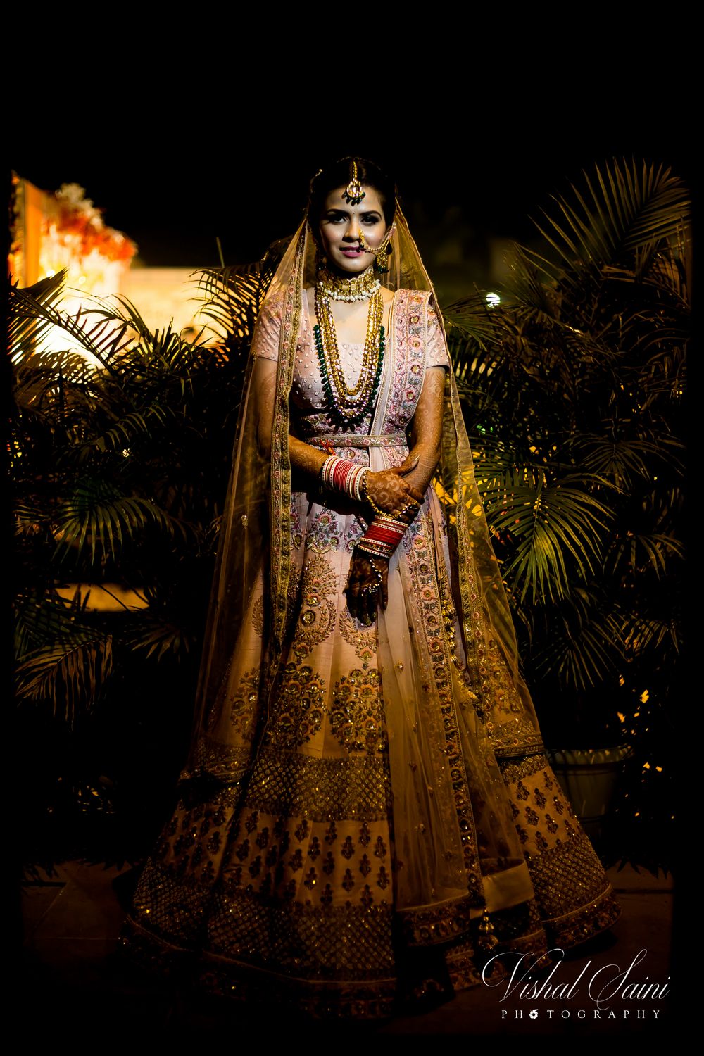 Photo of light pink bridal lehenga with contrasting green jewellery and waistbelt