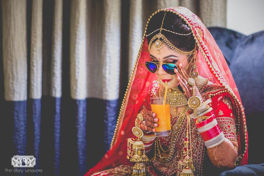 Photo of Bride in Red Lehenga Drinking Juice wearing Sunglasses
