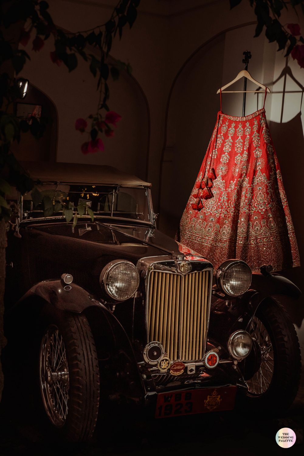 Photo of red bridal lehenga on hanger next to a vintage car