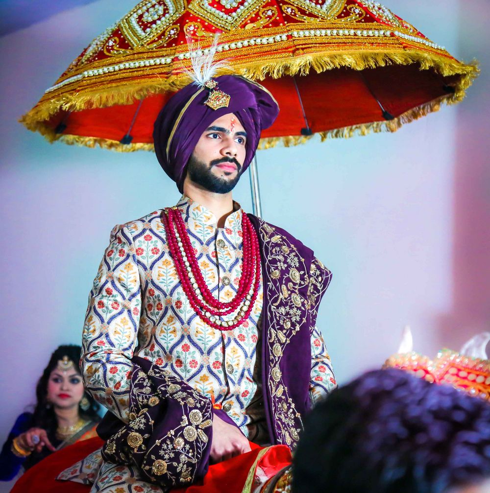 Photo of Groom wearing purple sherwani and turban with red beaded necklace