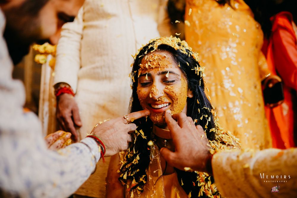 Photo of Bride smiling while getting smeared with Haldi.