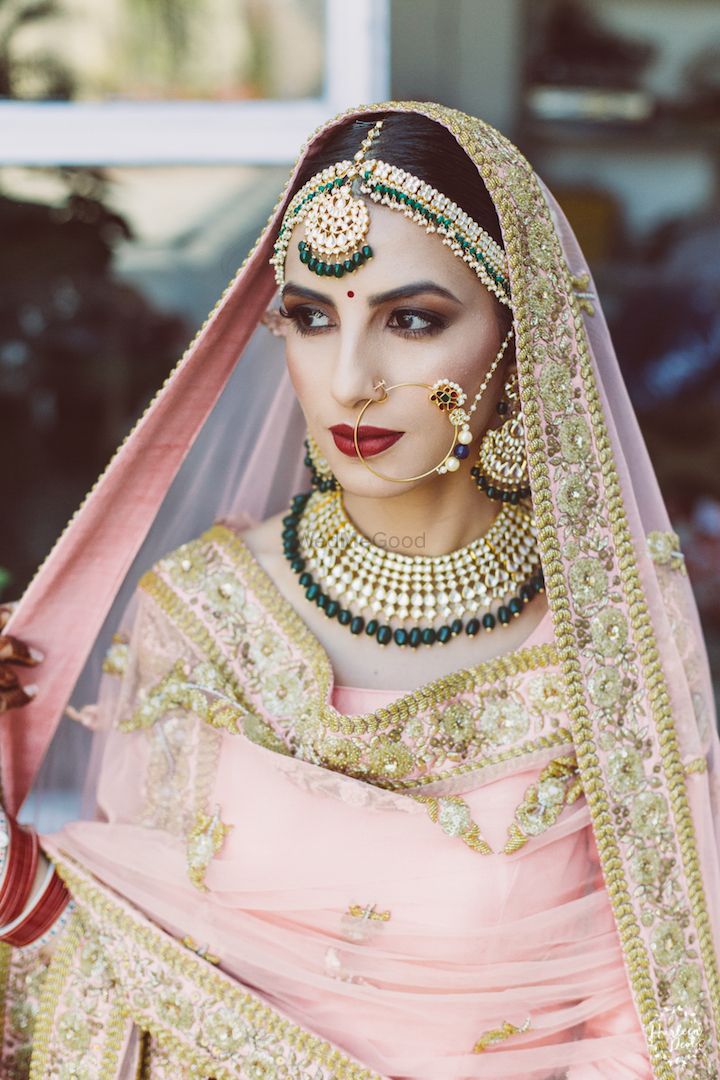 Photo of Bride posing in light pink lehenga and contrasting green jewellery