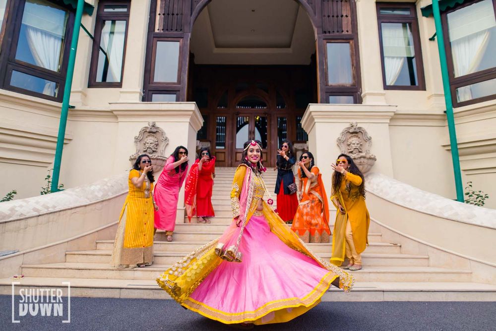 Photo of Bride twirling in yellow and pink lehenga with bridesmaids whistling