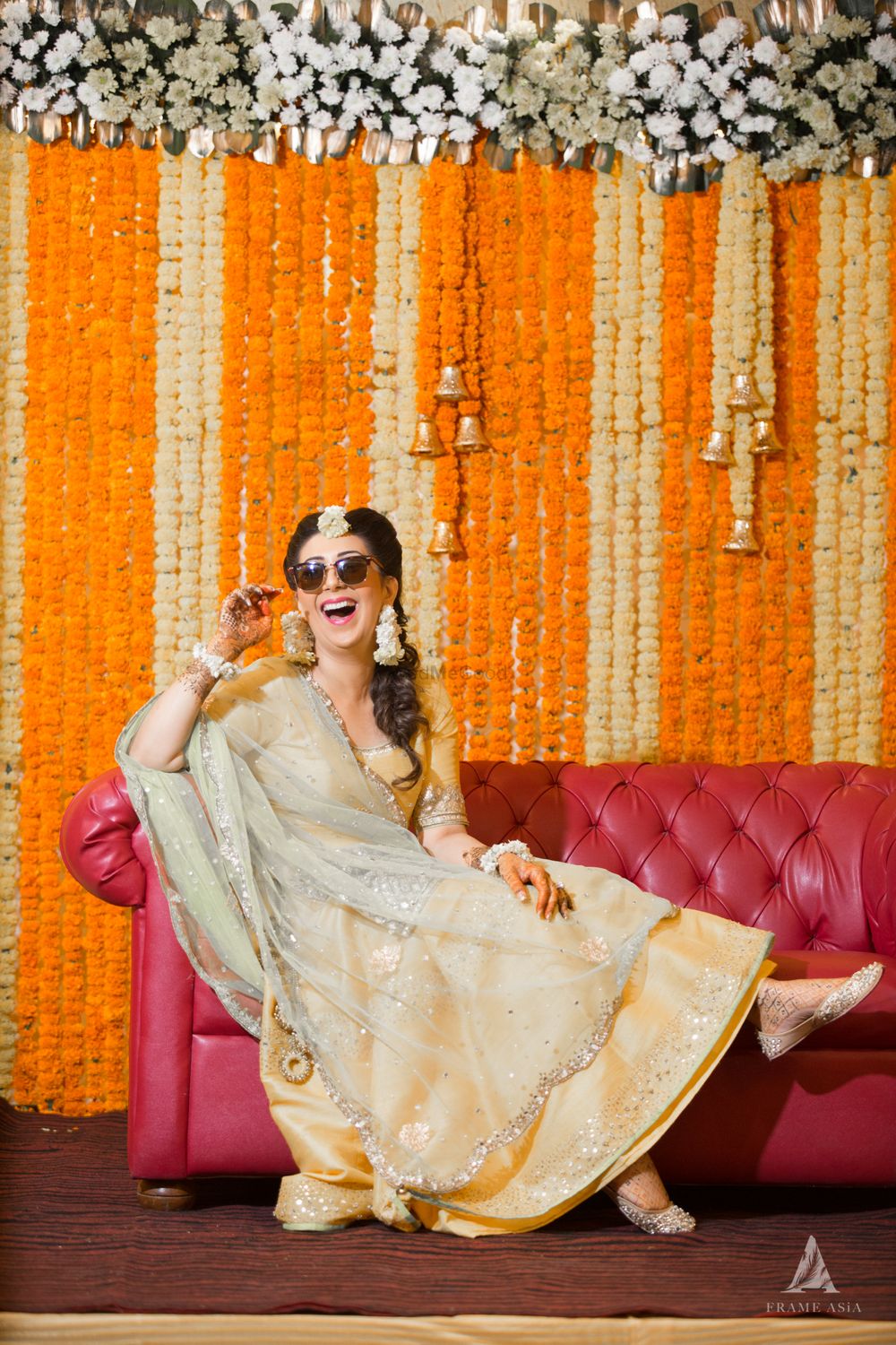 Photo of A bride to be poses on her mehendi in front of a marigold decor