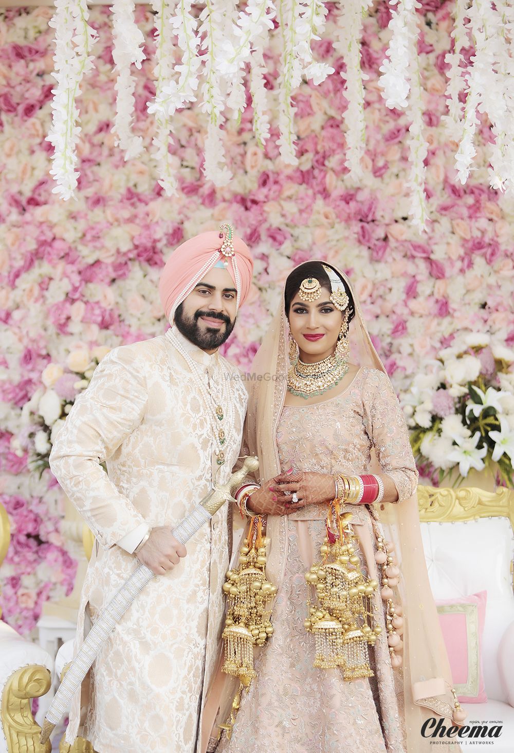 Photo of Coordinated Sikh bride and groom with floral wall backdrop