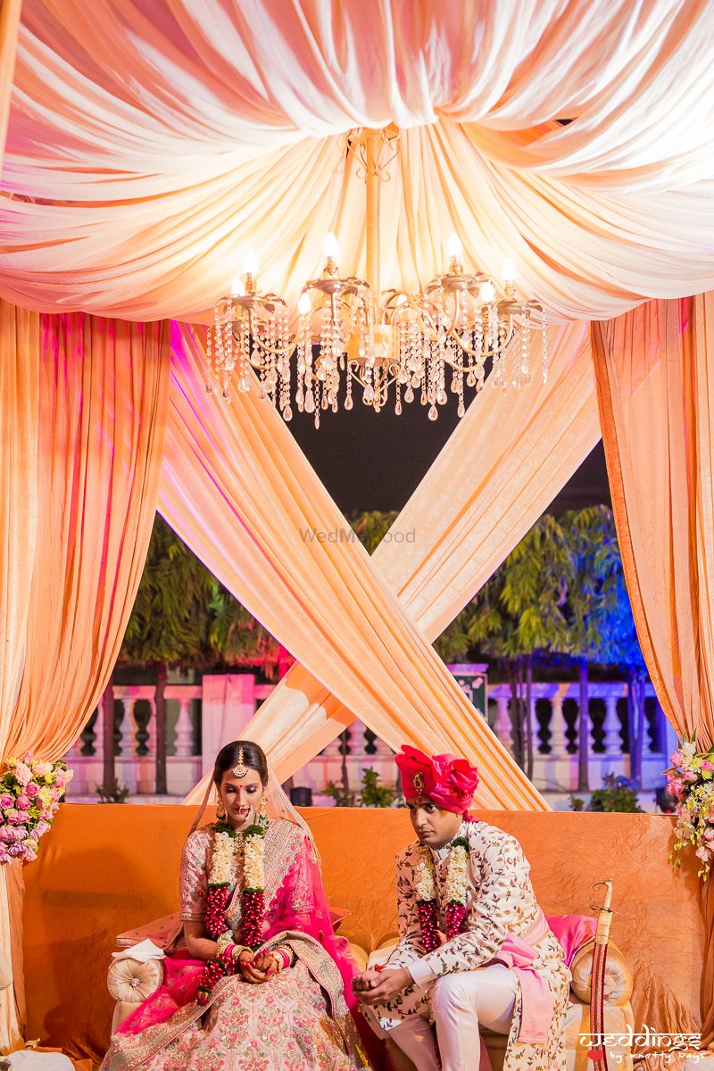 Photo of Peach mandap with drapes and chandeliers