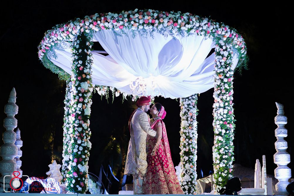 Photo of A bride and groom under a floral mandap.