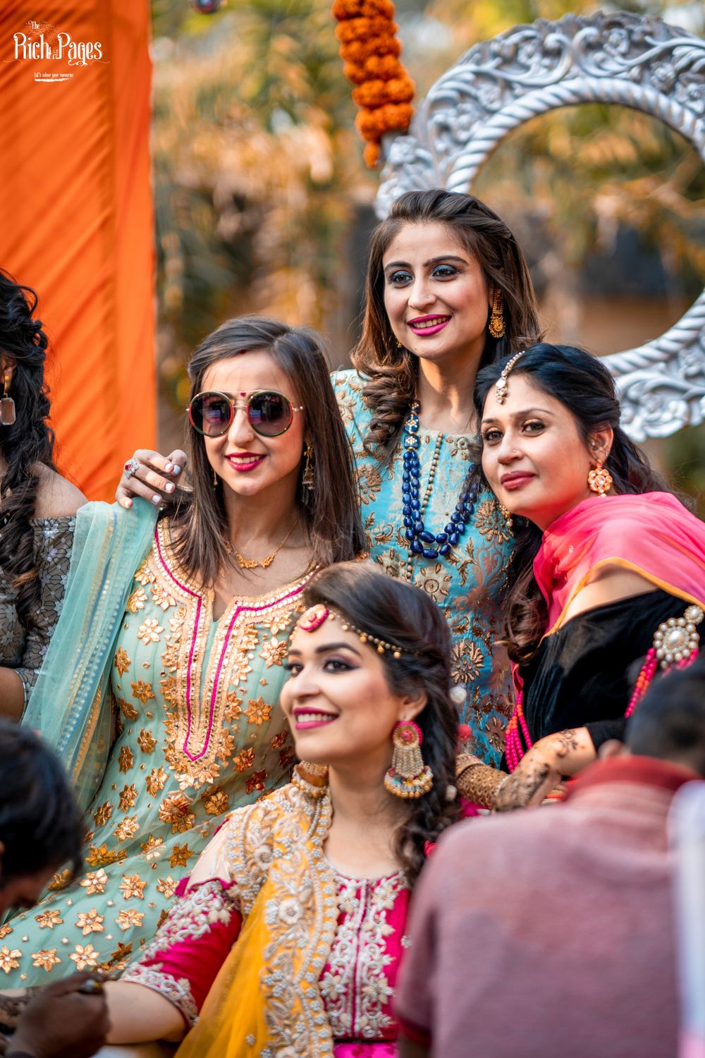 Photo of sisters and friends of the bride pose as the bride gets her mehendi done