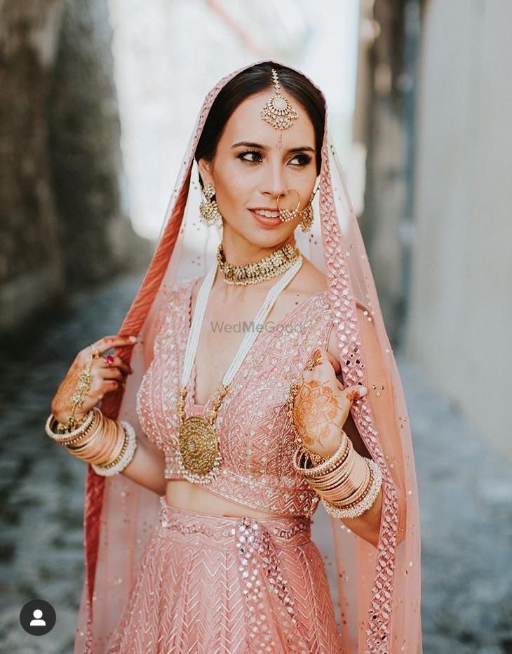 Photo of Bride wearing a pastel pink lehenga with statement haar.