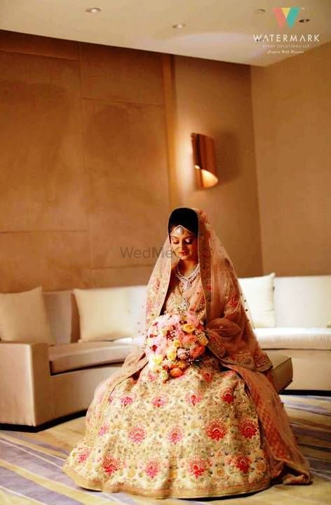 Photo of A bride in a floral lehenga sitting with a flower bouquet