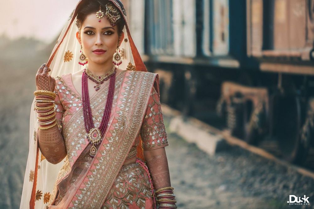 Photo of A bride in a pink lehenga and contrasting maroon colored jewels