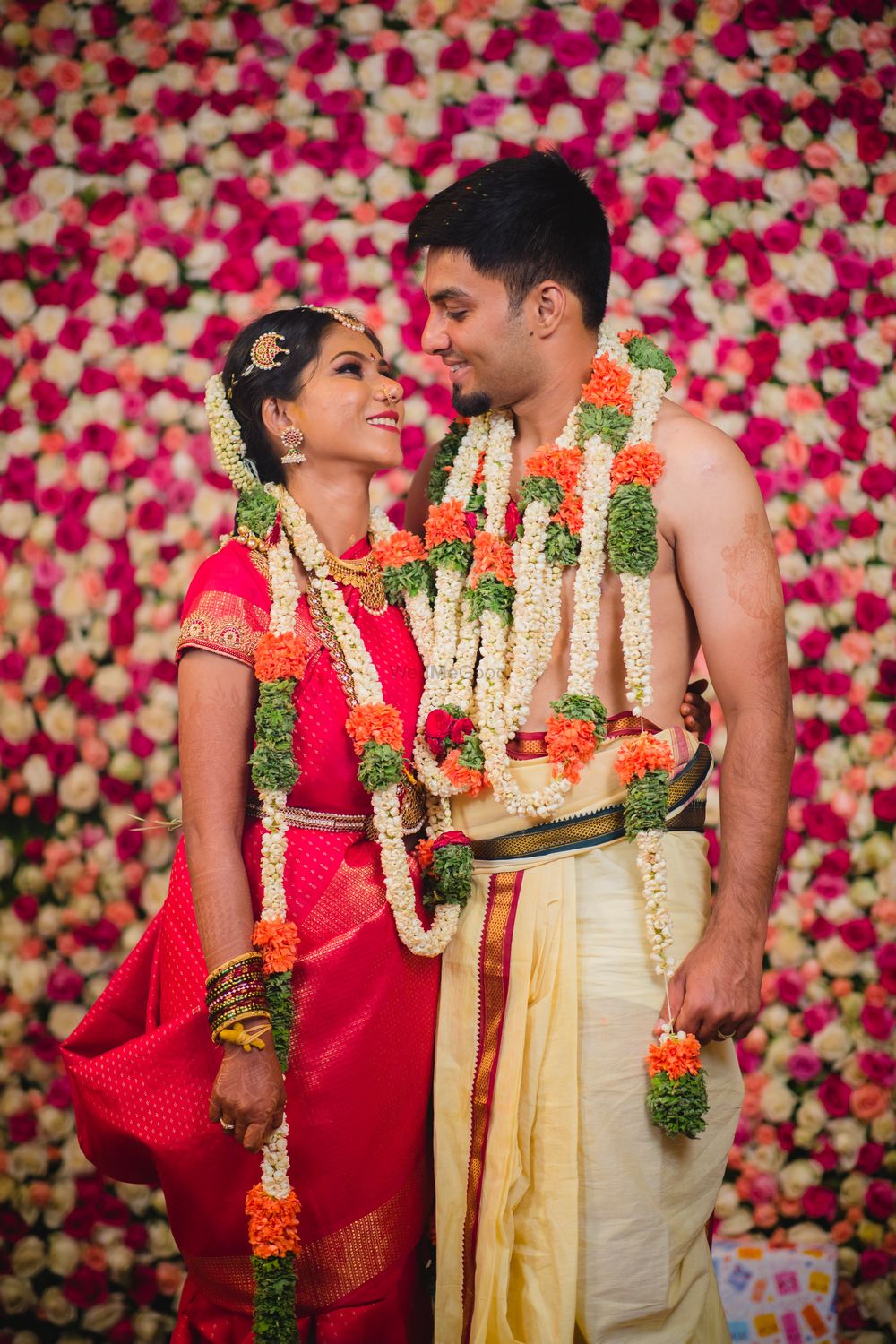 Photo of A south Indian couple pose infront of a floral wall with unique jaimalas