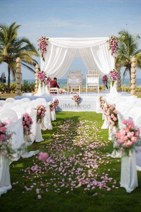 Photo of A white mandap setup with flowers and drapes