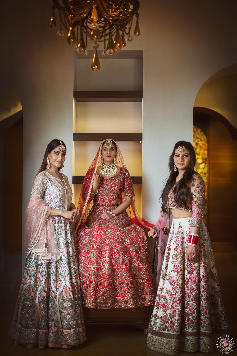 Photo of A bride in red lehenga poses with her bridesmaids on the wedding day