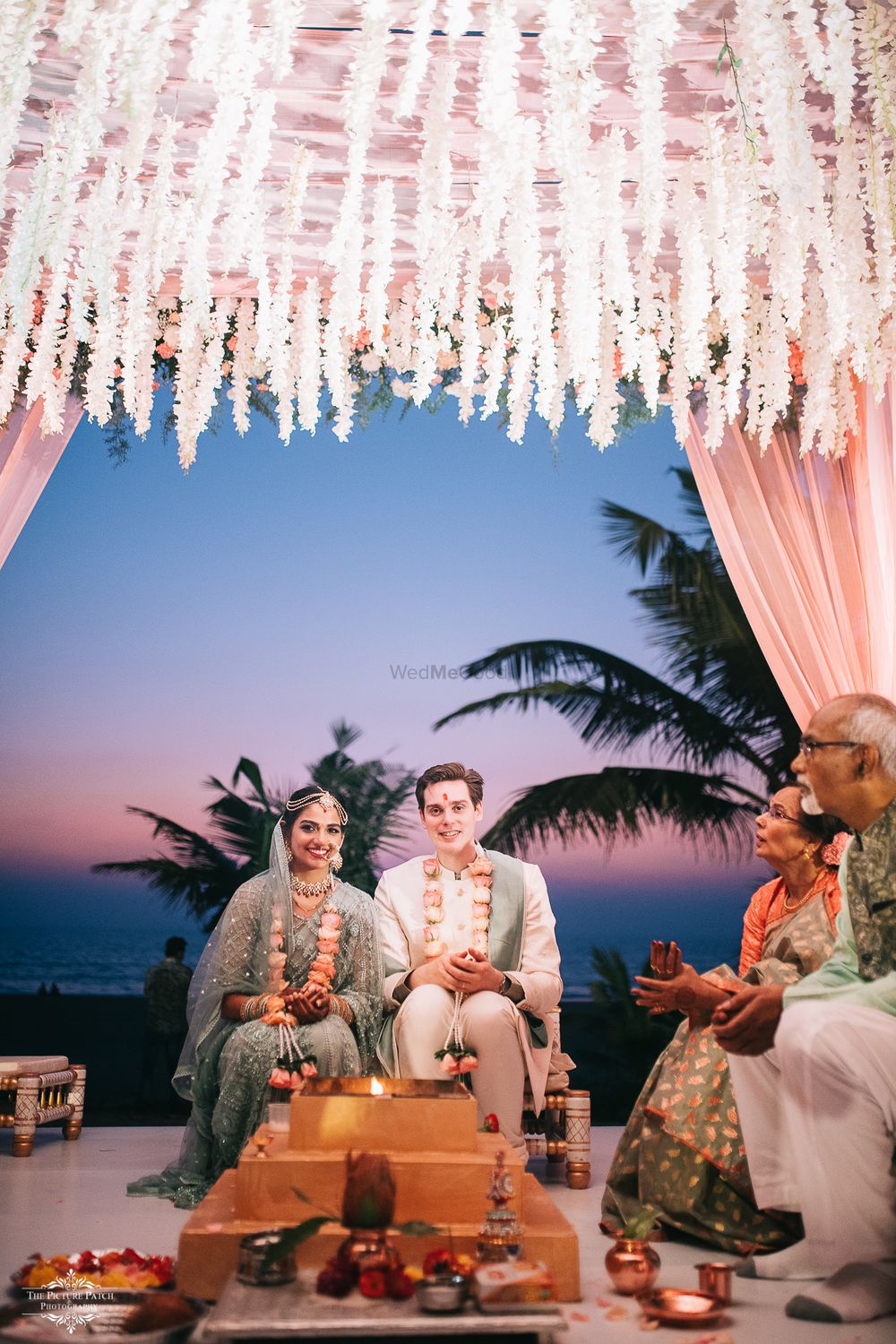 Photo of A couple sitting for their pheras in their white and pink mandap