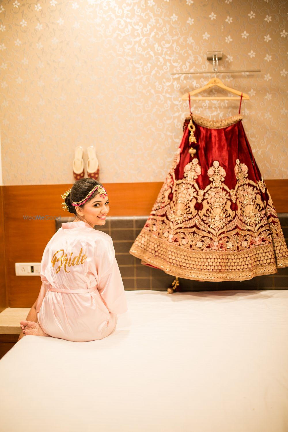 Photo of bride in robe with maroon velvet lehenga on hanger