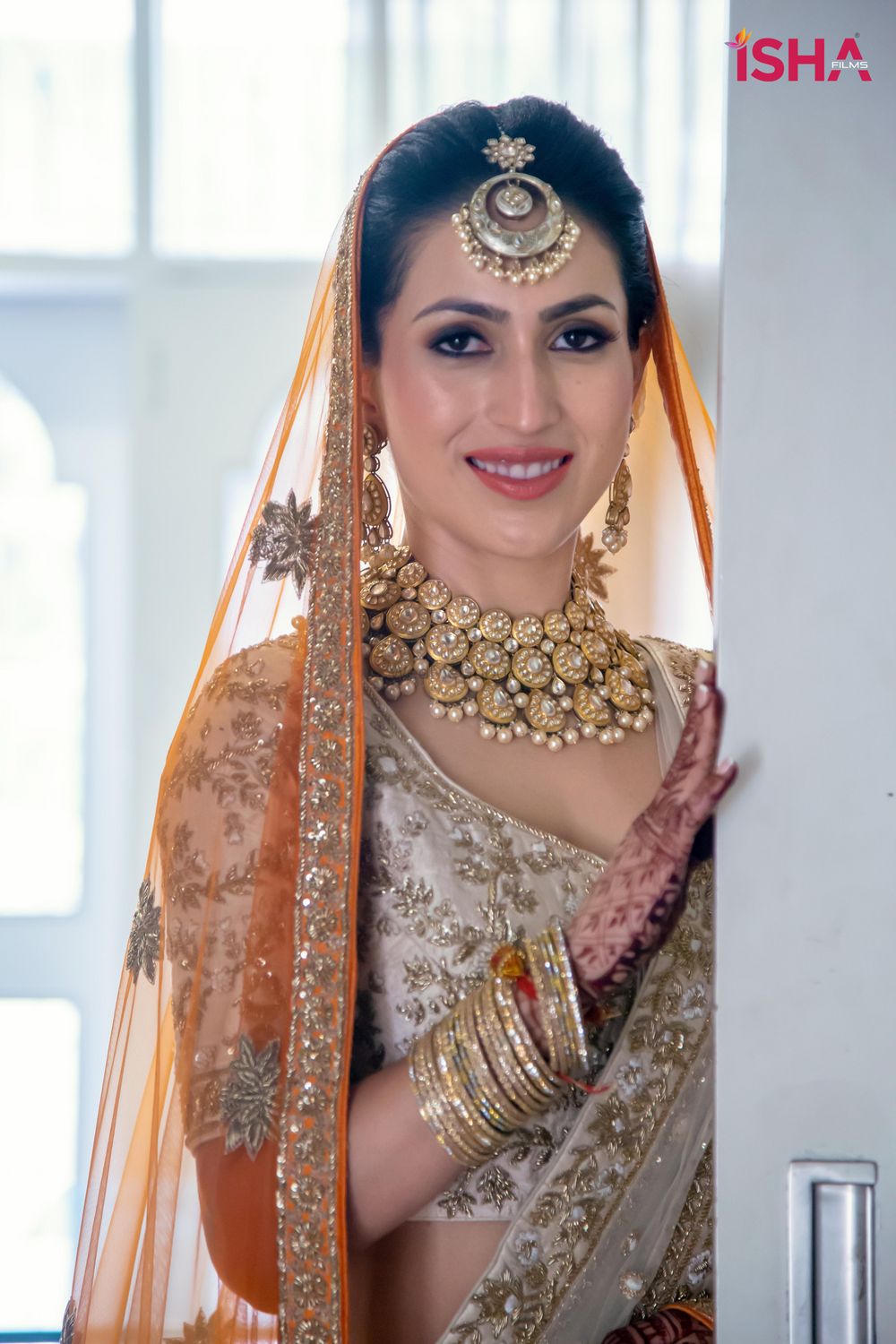 Photo of bride in an ivory and gold lehenga with orange second dupatta