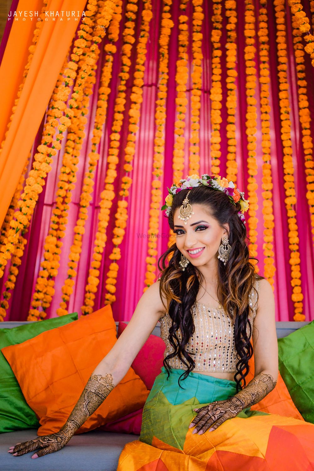 Photo of bride on mehendi seat with genda phool decor and floral wreath