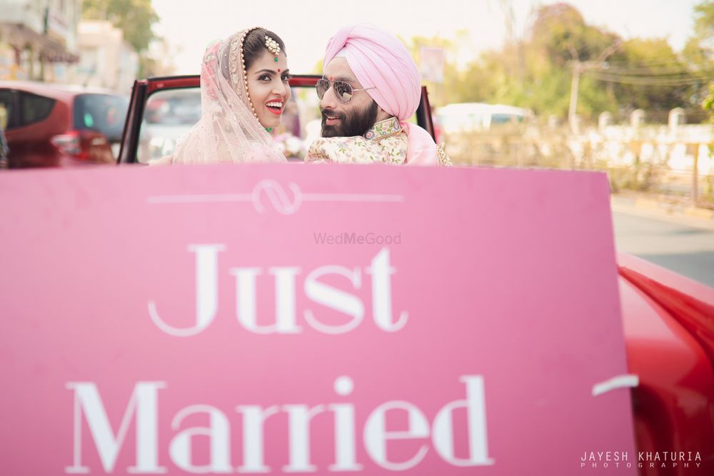 Photo of couple exit car with just married prop