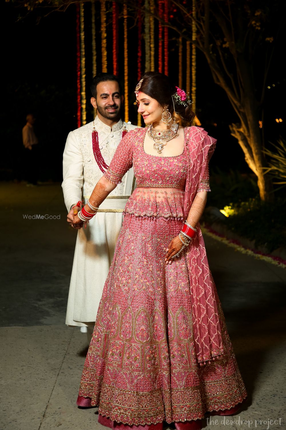 Photo of A bride in a pretty pink lehenga and groom in white sherwani.