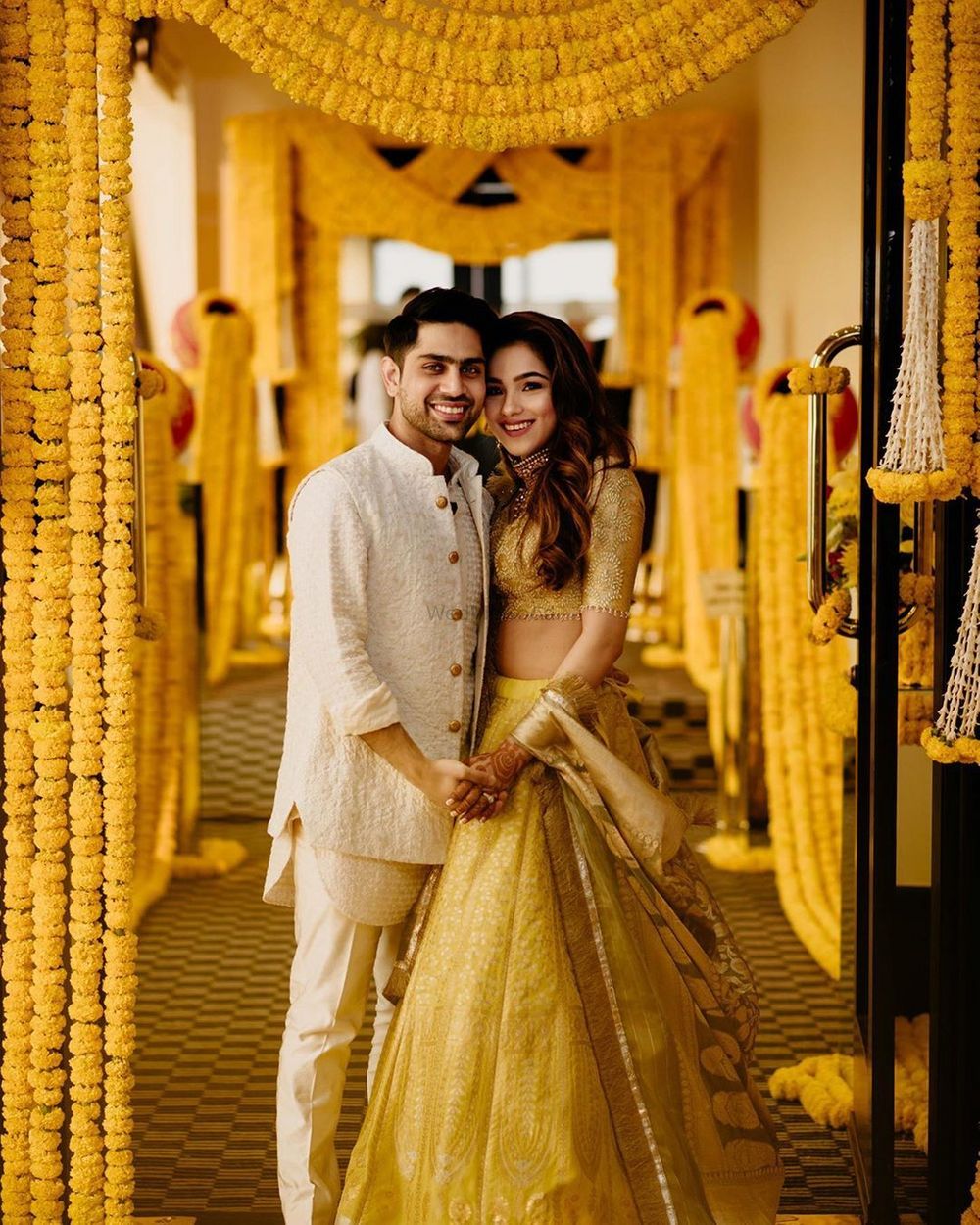 Photo of A bride and groom portrait with genda phool decor in the backdrop
