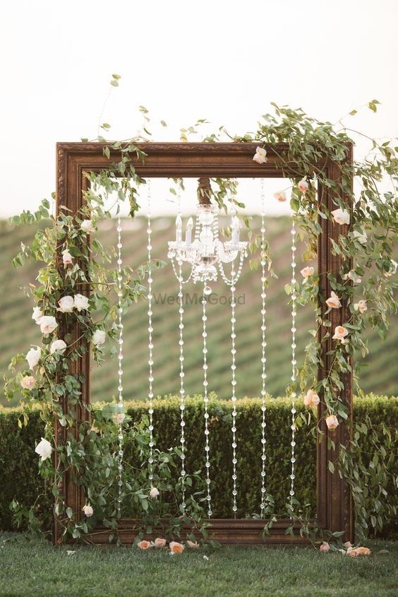 Photo of A huge wooden frame decorated with flowers and chandeliers for a photobooth.