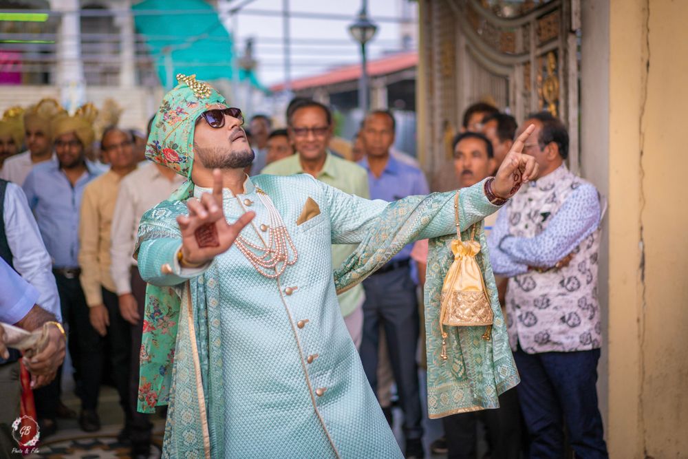 Photo of groom dancing while entering in light blue sherwani and floral safa
