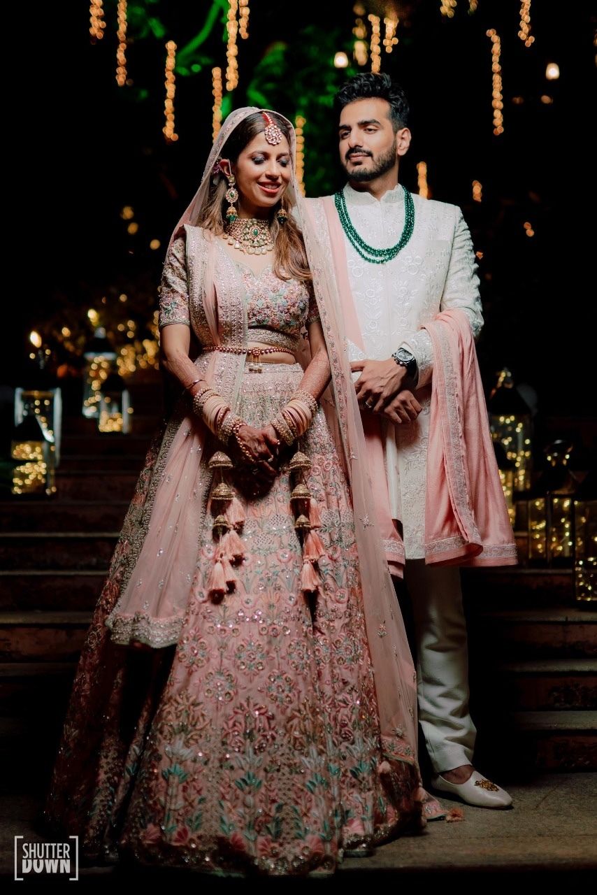 Photo of couple shot with bride in millennial pink lehenga with waistbelt
