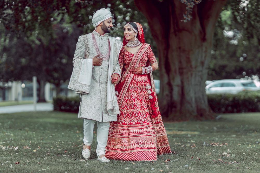 Photo of bride and groom in contrasting outfits with grey sherwani and red lehenga