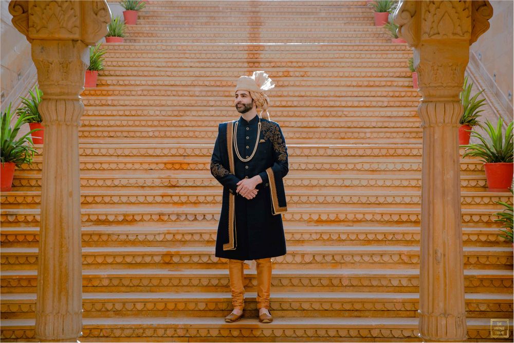 Photo of Groom wearing a navy blue sherwani with gold churidars and a beige safa.