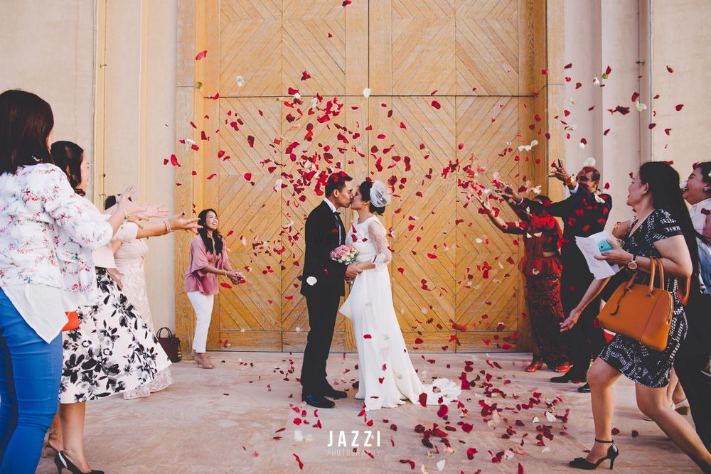 Photo of Couple kissing while guests shower rose petals