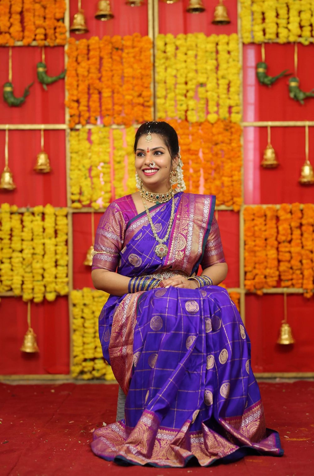 Photo of A south Indian bride sitting in front of a floral wall with marigolds