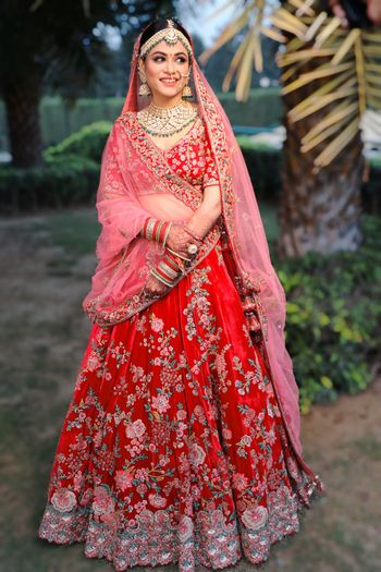 Photo of A picture of a happy bride dressed in red and pink bridal lehenga