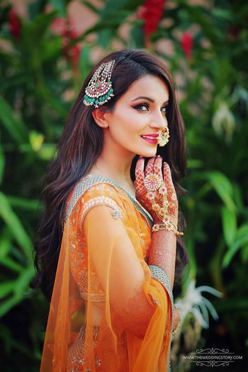 Bride in orange mehendi lehenga and unique jewellery