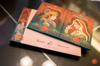 Photo of Modern Mughal theme wedding card with bride and groom portraits